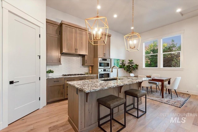 kitchen with a sink, gas stovetop, a chandelier, backsplash, and light wood-style floors