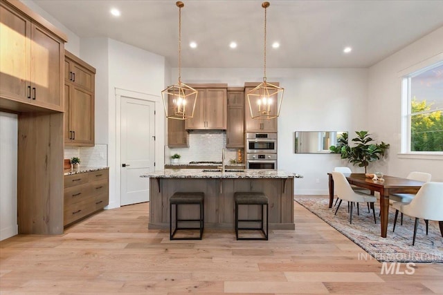 kitchen featuring stainless steel double oven, decorative backsplash, a sink, a center island with sink, and a chandelier