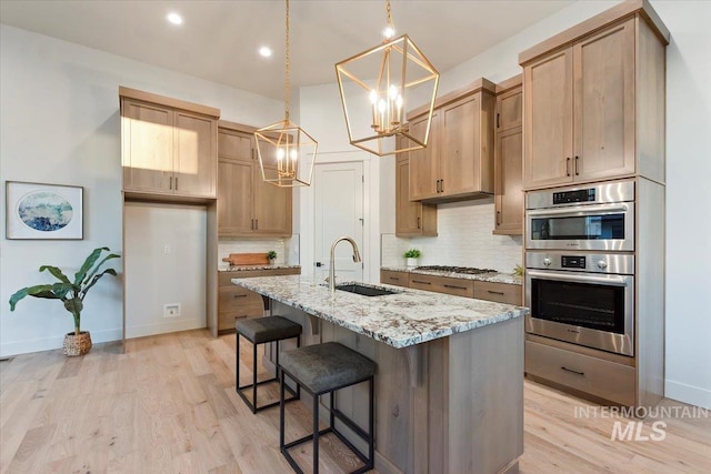 kitchen with a sink, a chandelier, stainless steel appliances, tasteful backsplash, and light stone counters