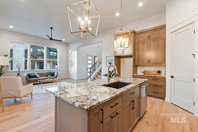 kitchen featuring a sink, stainless steel dishwasher, light wood finished floors, tasteful backsplash, and decorative light fixtures