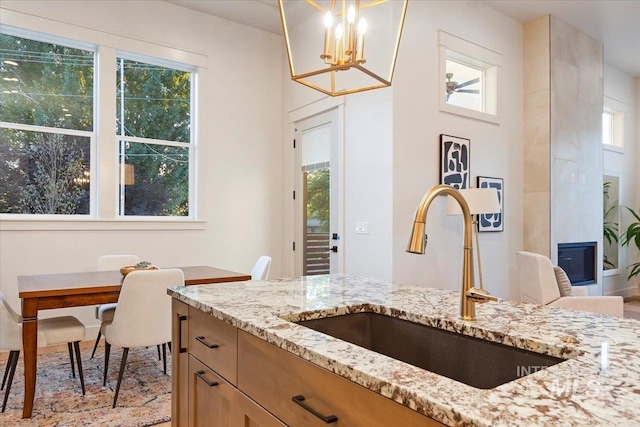 kitchen featuring a sink, light stone counters, a chandelier, hanging light fixtures, and light brown cabinetry