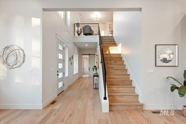 foyer featuring stairs, baseboards, a barn door, a towering ceiling, and light wood-type flooring