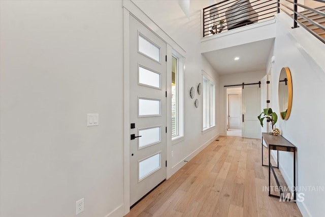entrance foyer with a barn door, light wood-style floors, and baseboards