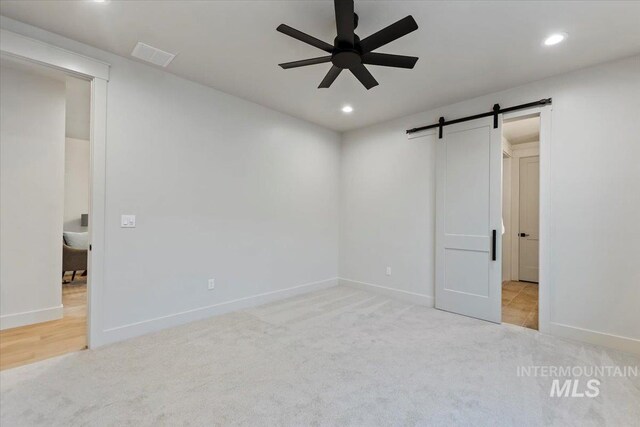 carpeted empty room featuring ceiling fan, a barn door, recessed lighting, and baseboards