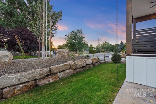 yard at dusk featuring a lawn