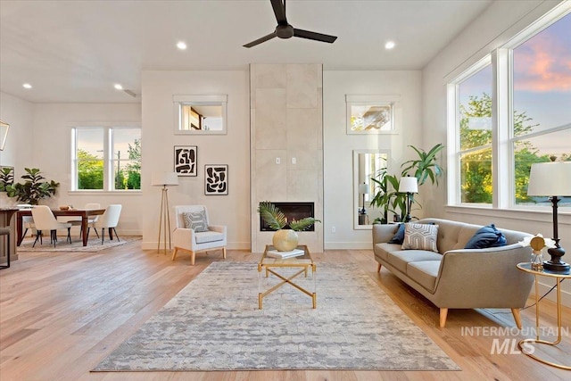 living room featuring a ceiling fan, light wood-style floors, recessed lighting, baseboards, and a fireplace