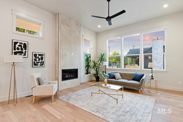 living room with ceiling fan, a fireplace, light wood finished floors, baseboards, and healthy amount of natural light