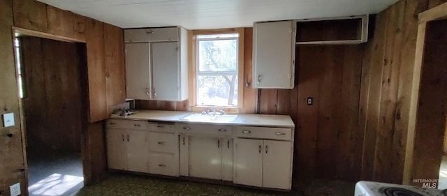 kitchen featuring wooden walls, a wealth of natural light, sink, and white cabinets