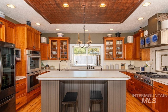 8344 Partridge Dr, Nampa, ID 83686 - kitchen featuring light wood finished floors, a center island, brown cabinetry, light countertops, and appliances with stainless steel finishes