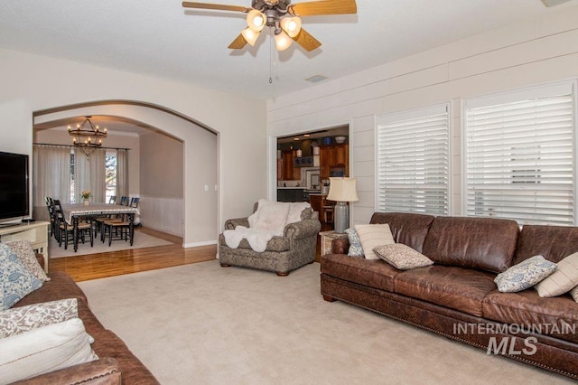 8344 Partridge Dr, Nampa, ID 83686 - carpeted living room featuring arched walkways, visible vents, wood walls, and ceiling fan with notable chandelier