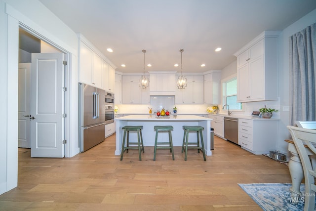 kitchen with light hardwood / wood-style flooring, stainless steel appliances, a center island, and white cabinetry