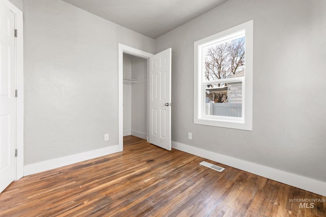 unfurnished bedroom with hardwood / wood-style floors, a closet, visible vents, and baseboards