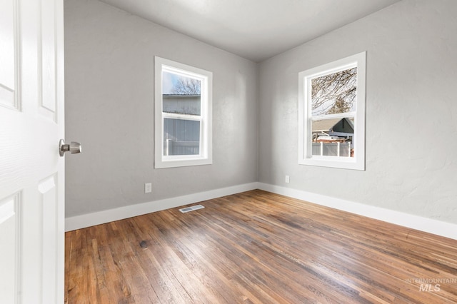 unfurnished room with hardwood / wood-style flooring, visible vents, and baseboards