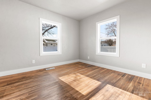 empty room with a healthy amount of sunlight, baseboards, visible vents, and wood finished floors