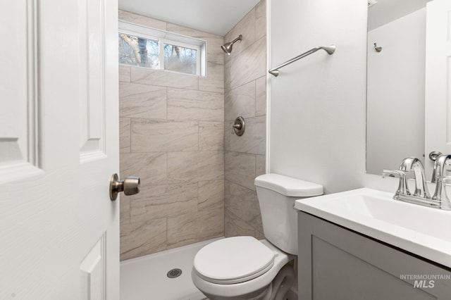 full bathroom featuring toilet, a tile shower, and vanity