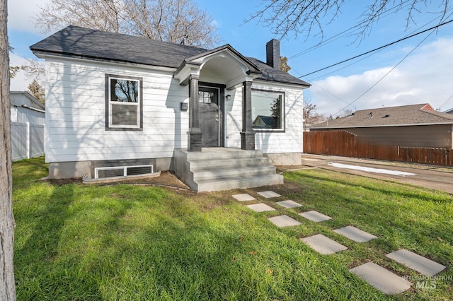 bungalow-style house with a chimney, fence, and a front lawn