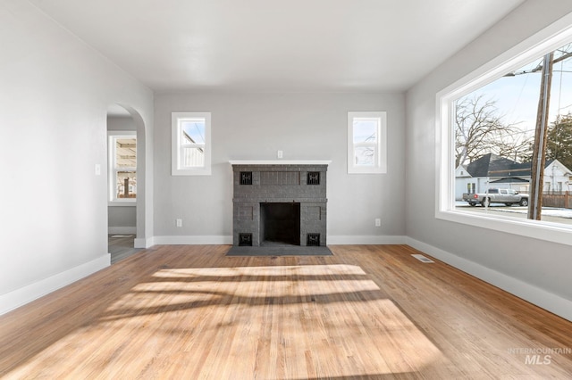 unfurnished living room featuring a brick fireplace, a healthy amount of sunlight, and wood finished floors