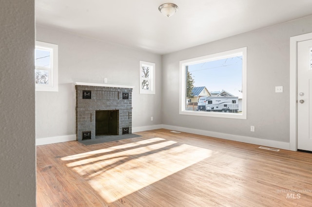 unfurnished living room featuring a brick fireplace, visible vents, baseboards, and wood finished floors