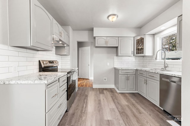 kitchen with under cabinet range hood, stainless steel appliances, a sink, gray cabinets, and glass insert cabinets