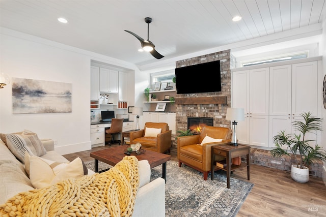 living room with recessed lighting, a fireplace, baseboards, light wood-style floors, and built in study area