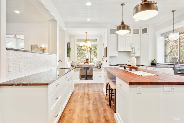 kitchen with tasteful backsplash, white cabinets, butcher block counters, glass insert cabinets, and hanging light fixtures