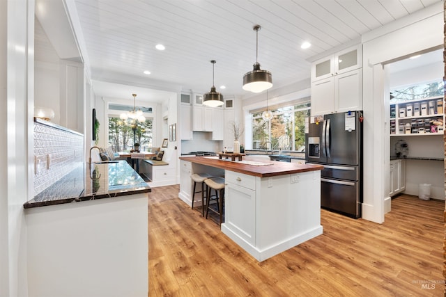 kitchen featuring butcher block counters, a kitchen island, white cabinetry, stainless steel refrigerator with ice dispenser, and glass insert cabinets