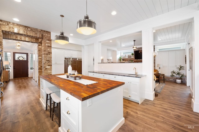 kitchen featuring a center island, butcher block counters, hanging light fixtures, white cabinets, and a sink