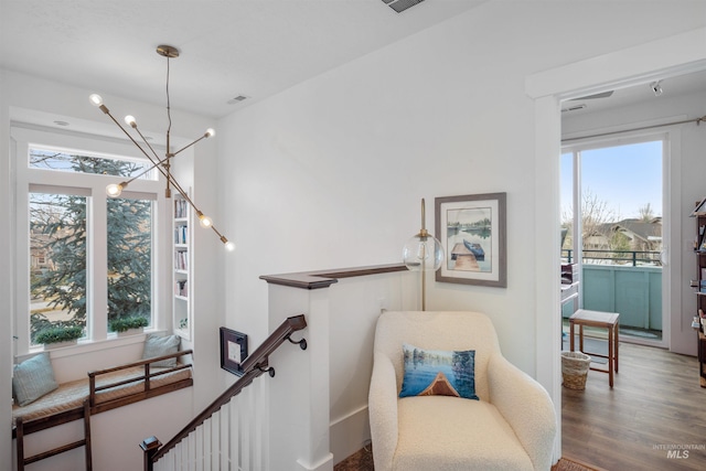 sitting room featuring a healthy amount of sunlight, a notable chandelier, an upstairs landing, and wood finished floors