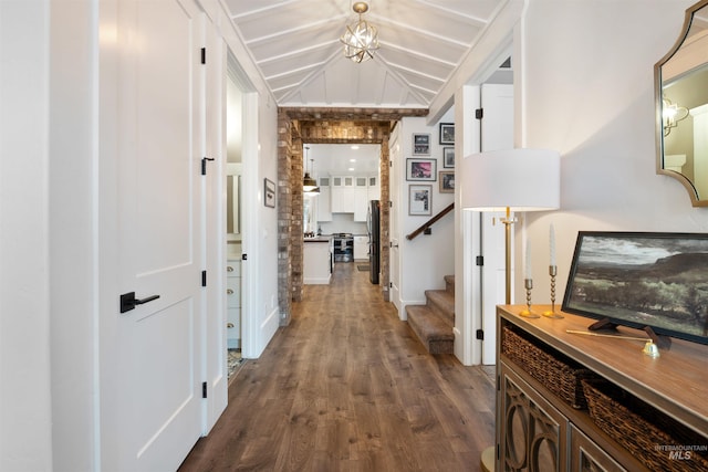 hall featuring dark wood-style floors, stairs, vaulted ceiling, and an inviting chandelier