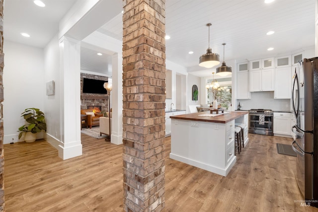 kitchen featuring a center island, decorative light fixtures, stainless steel appliances, glass insert cabinets, and butcher block countertops