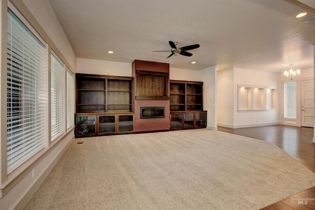 unfurnished living room featuring ceiling fan with notable chandelier, wood-type flooring, and a wealth of natural light