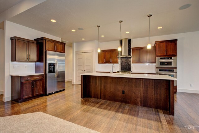 kitchen featuring wall chimney exhaust hood, backsplash, wood-type flooring, decorative light fixtures, and appliances with stainless steel finishes