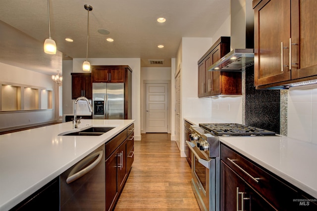 kitchen featuring pendant lighting, wall chimney range hood, sink, light hardwood / wood-style flooring, and stainless steel appliances