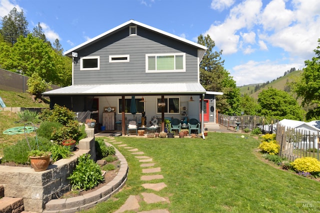 back of house with metal roof, fence, a patio area, and a lawn