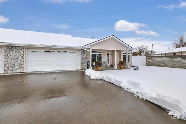 view of front of property featuring stone siding, stucco siding, driveway, and fence