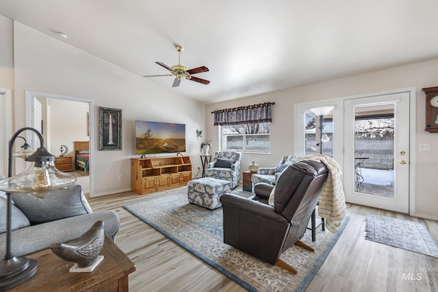 living area with baseboards, lofted ceiling, a ceiling fan, and light wood finished floors