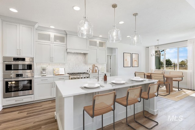7029 S Tindaris Ave, Meridian, ID 83642 - kitchen featuring stainless steel appliances, light wood finished floors, recessed lighting, tasteful backsplash, and light countertops
