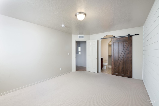 unfurnished bedroom with a barn door, a textured ceiling, carpet floors, and visible vents