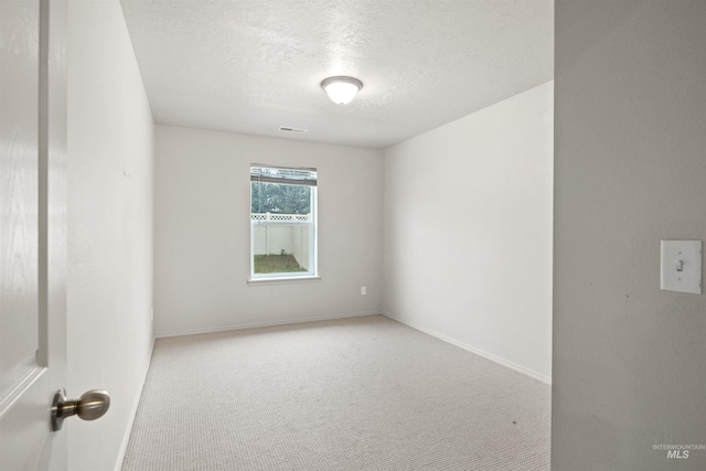 carpeted spare room featuring a textured ceiling, visible vents, and baseboards