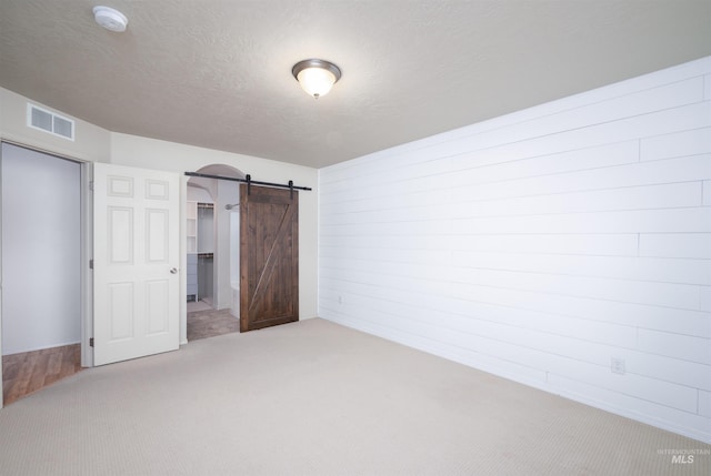unfurnished bedroom featuring a barn door, a textured ceiling, wooden walls, carpet, and visible vents