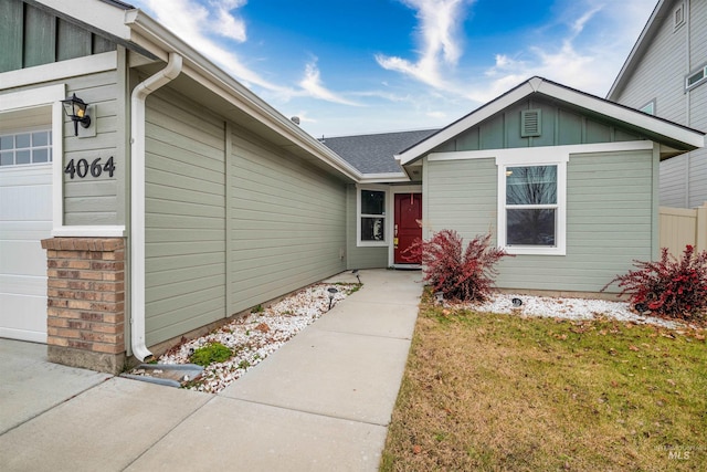 property entrance with a garage, a lawn, and board and batten siding