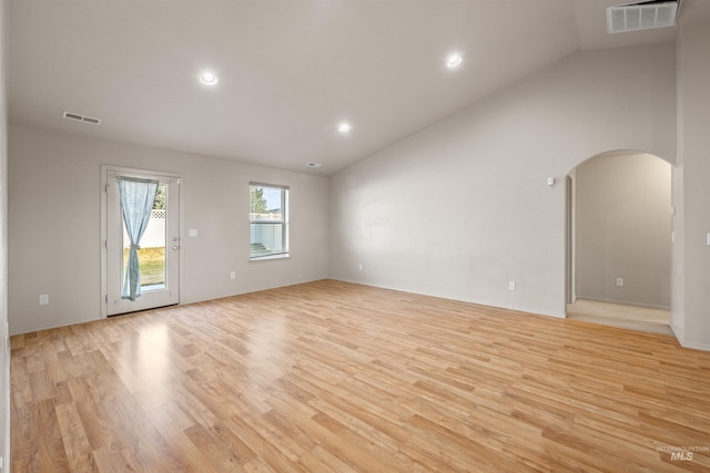 unfurnished living room with arched walkways, vaulted ceiling, visible vents, and light wood-style flooring