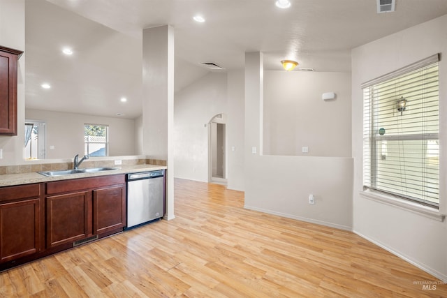 kitchen featuring light countertops, stainless steel dishwasher, a sink, arched walkways, and light wood-style floors
