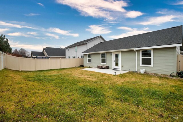 rear view of house with fence, a lawn, a shingled roof, and a patio