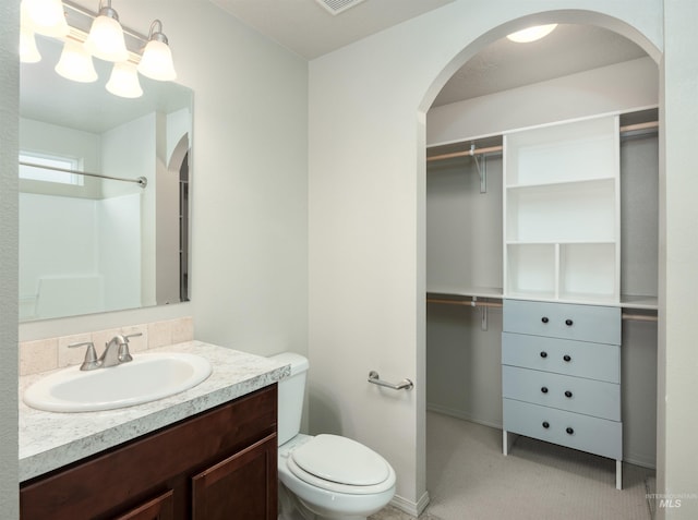 bathroom with a walk in closet, toilet, vanity, and visible vents