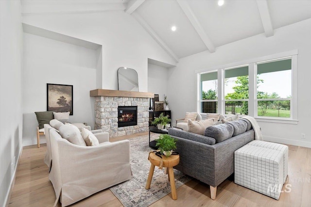 living area featuring light wood finished floors, beamed ceiling, a stone fireplace, and baseboards