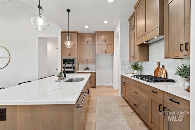 kitchen featuring backsplash, light stone countertops, an island with sink, appliances with stainless steel finishes, and a sink