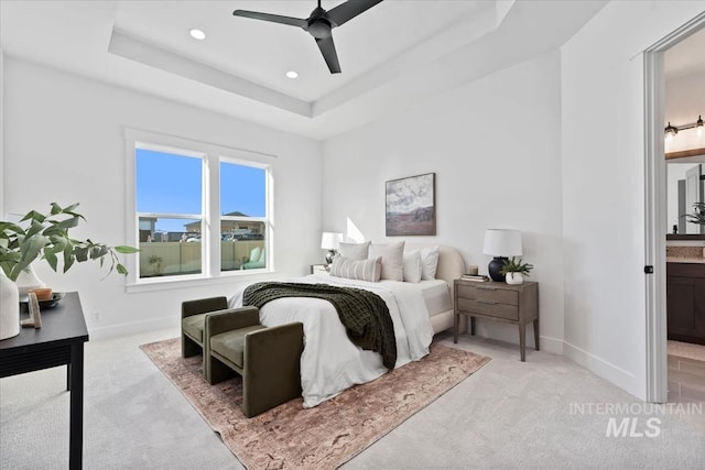 bedroom with light carpet, ensuite bathroom, a tray ceiling, recessed lighting, and baseboards