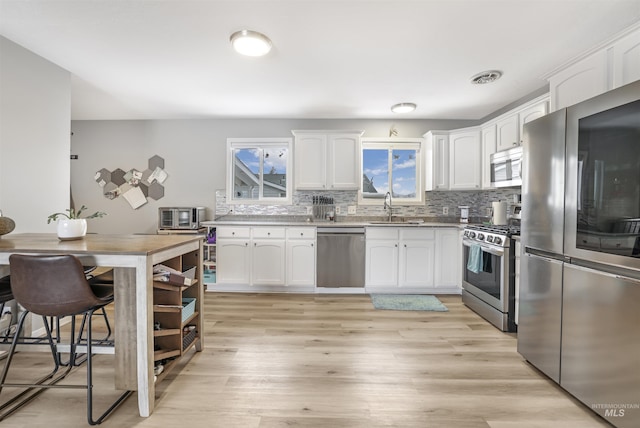 kitchen with sink, light wood-type flooring, stainless steel appliances, white cabinets, and tasteful backsplash