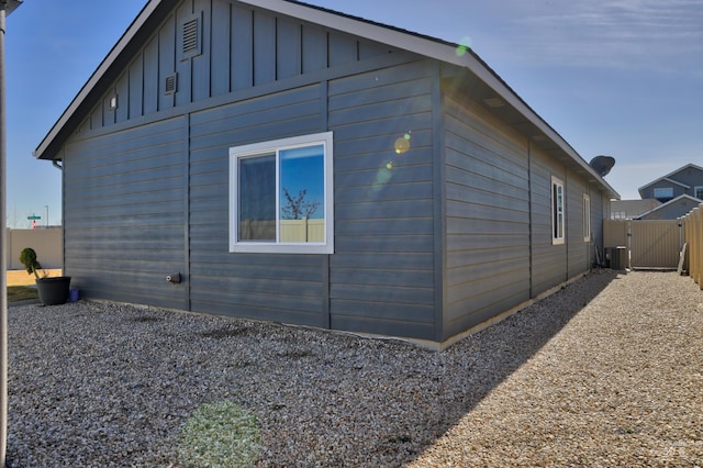 view of side of property with central AC, board and batten siding, fence, and a gate